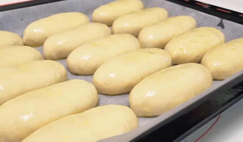 Сырые пирожки на противне перед выпечкой, смазанные желтком для румяной корочки