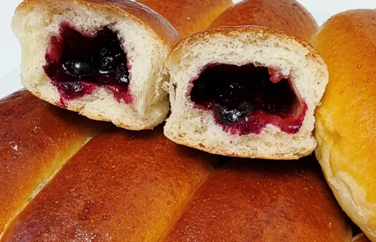 Домашние пышные пирожки с замороженной смородиной и повидлом в разрезе на противне