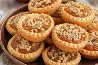 Золотистые корзиночки из песочного теста с яблочной начинкой и грецким орехом на тарелке.