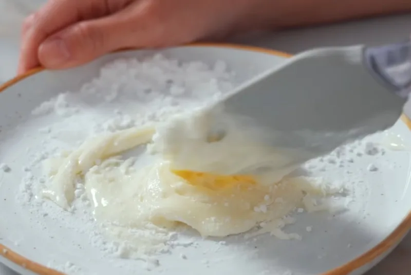 Смешивание сгущенного молока и сахарной пудры венчиком в миске