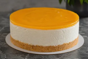 Слоистый чизкейк без выпечки: песочная основа, белый творожный слой и яркое оранжевое апельсиновое желе сверху