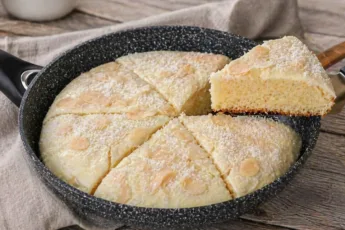 Белоснежный торт с кокосовой стружкой и белой глазурью, нарезанный на порции прямо в сковороде