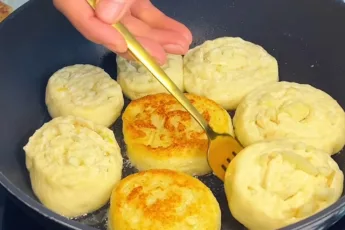 Золотистые круглые творожные булочки с кусочками яблок внутри слоев, обжаренные на сковороде