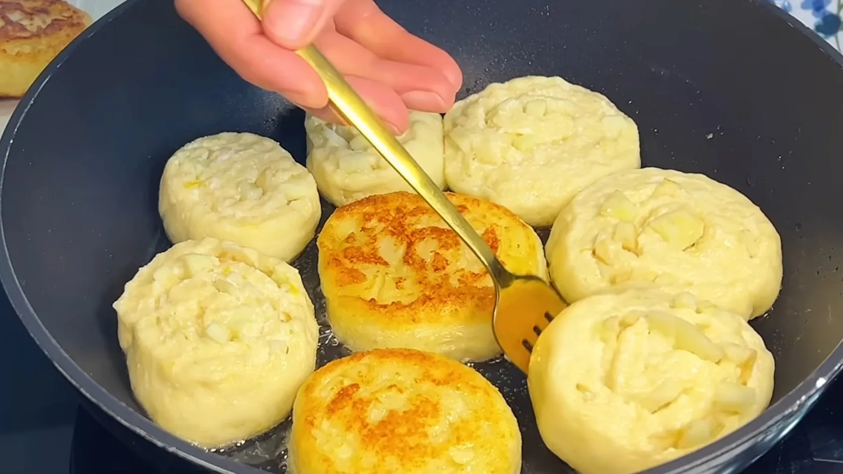 Золотистые круглые творожные булочки с кусочками яблок внутри слоев, обжаренные на сковороде