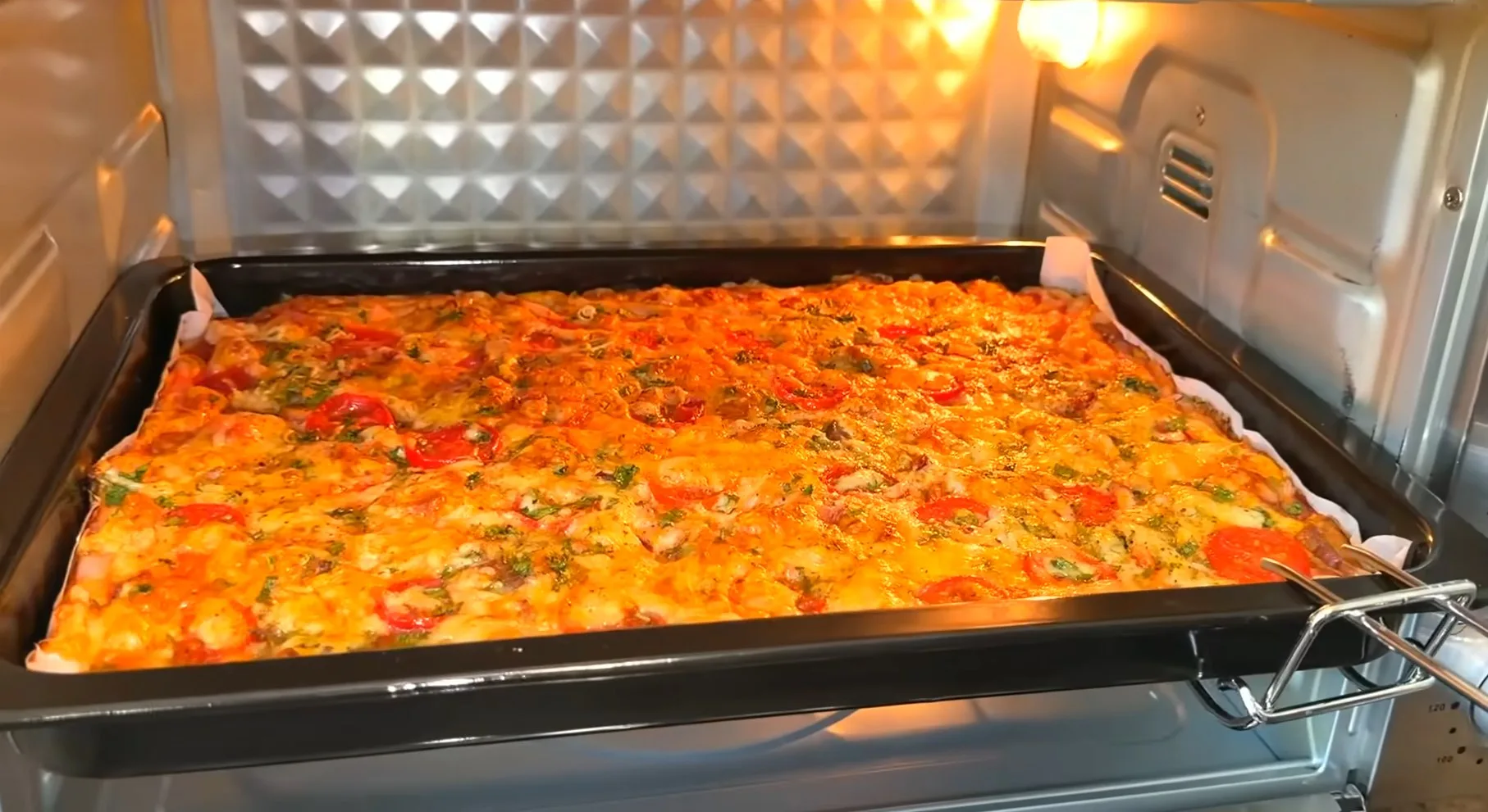 Большая румяная домашняя пицца с кусочками ветчины, половинками черри и расплавленным сыром