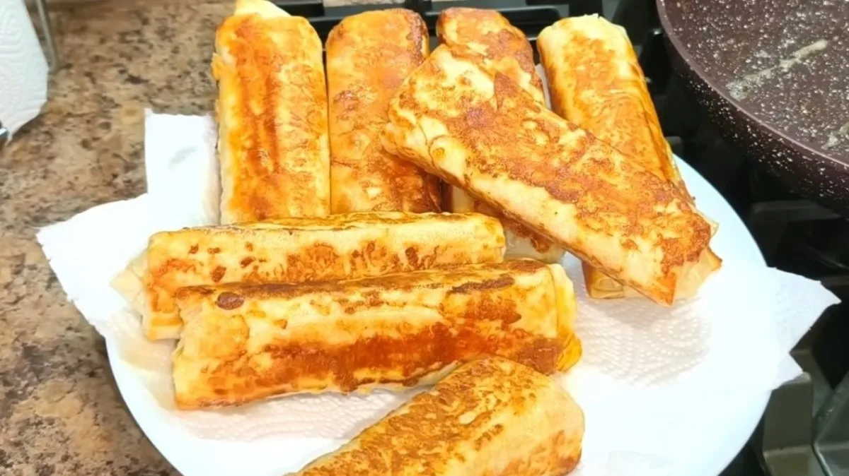 Золотистые обжаренные рулетики из лаваша с начинкой, разложенные на тарелке