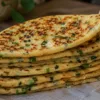 Стопка румяных полукруглых лепешек-кармашков с зеленью на тарелке