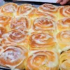 Пышные круглые булочки-улитки на противне, густо политые сверху густым белым творожным кремом