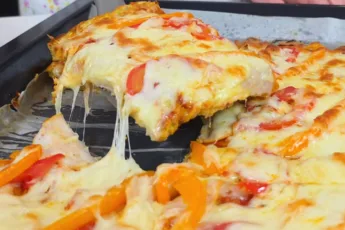 Большой прямоугольный противень с румяной кабачковой пиццей, покрытой кусочками ветчины, перца и толстым слоем расплавленного золотистого сыра