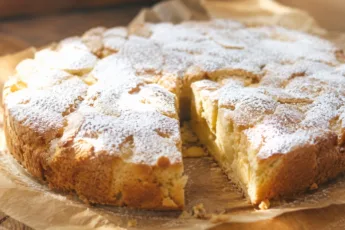 Готовая шарлотка с яблоками на круглом блюде с золотистой корочкой