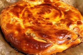 Гуштли катлама на противне — слоёная лепёшка с видимыми слоями теста и мясной начинкой, посыпанная кунжутом