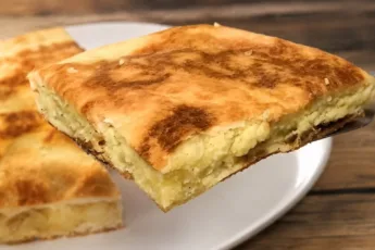 Румяная хрустящая запеканка из лаваша с картофельно-яичной начинкой на сковороде, разрезанная на порции