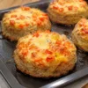 Большой противень, уставленный пышными круглыми мясными котлетами с высокой румяной шапкой из расплавленного золотистого сыра, кусочков красного помидора и ароматных зеленых трав