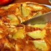 Круглый пышный яблочный пирог золотистого цвета на сковороде, верхний слой которого состоит из веера мягких карамельных долек яблок, слегка присыпанных корицей