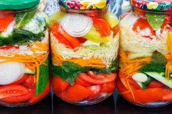 Разноцветные слои маринованных овощей с зеленью и чесноком в прозрачной стеклянных банках на зиму