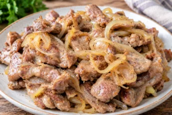 Золотистые жареные куриные желудки с луком на тарелке