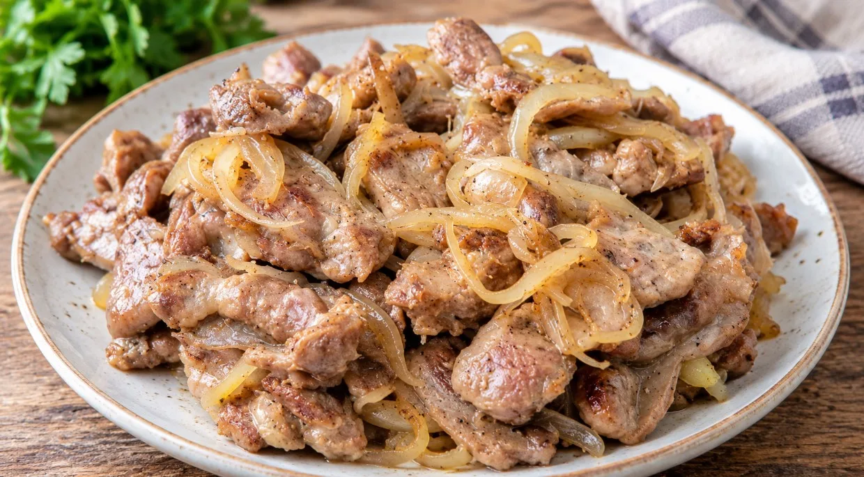 Золотистые жареные куриные желудки с луком на тарелке