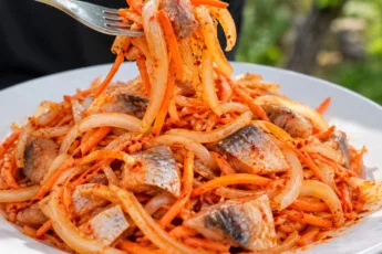 Аппетитная пикантная селедка по-корейски в миске, кусочки рыбы перемешаны с тонкими полукольцами лука и тертой морковью в густом красном томатном маринаде