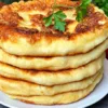 Стопка румяных золотистых лепешек с картофельной начинкой на тарелке, обильно смазанных растопленным сливочным маслом