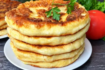 Стопка румяных золотистых лепешек с картофельной начинкой на тарелке, обильно смазанных растопленным сливочным маслом