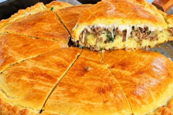 Аппетитный кусочек мясного пирога в разрезе, видны слои из нежного картофельного пюре, сочного мясного фарша с луком и расплавленного желтого сыра