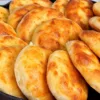 Огромная высокая гора румяных золотистых домашних мини-лепешек круглой формы, разложенных на столе
