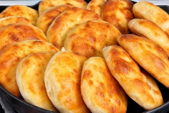 Огромная высокая гора румяных золотистых домашних мини-лепешек круглой формы, разложенных на столе