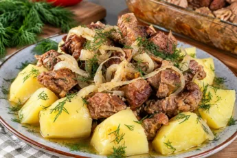 Запеченная свинина с луком на тарелке с картофелем, видна румяная корочка и сочная текстура мяса