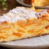 Отрезанный порционный кусочек нежного творожно-тыквенного пирога на тарелке, внутри видна красивая слоистая структура из тонких янтарных пластинок тыквы и белой белковой заливки, верхушка десерта слегка присыпана мелкой кокосовой стружкой