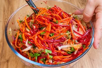 Яркий салат из тонкой соломки свежей свеклы и моркови с золотистым луком и зеленью в глубокой миске