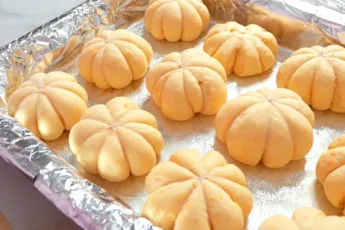 Процесс формовки домашних тыквенных булочек, сырой золотистый колобок дрожжевого теста аккуратно перевязан белой кулинарной нитью для создания рельефных секций на противне