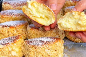 Процесс разламывания руками пышной домашней булочки «Лакомка», крупным планом виден воздушный мякиш дрожжевого теста, много густого заварного крема и обсыпка из ореховой крошки