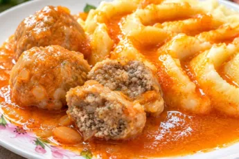 Советские мясные тефтели по ГОСТу с густым красным соусом и воздушным картофельным пюре, одна тефтелина на переднем плане разломлена пополам, демонстрируя сочный мясной фарш
